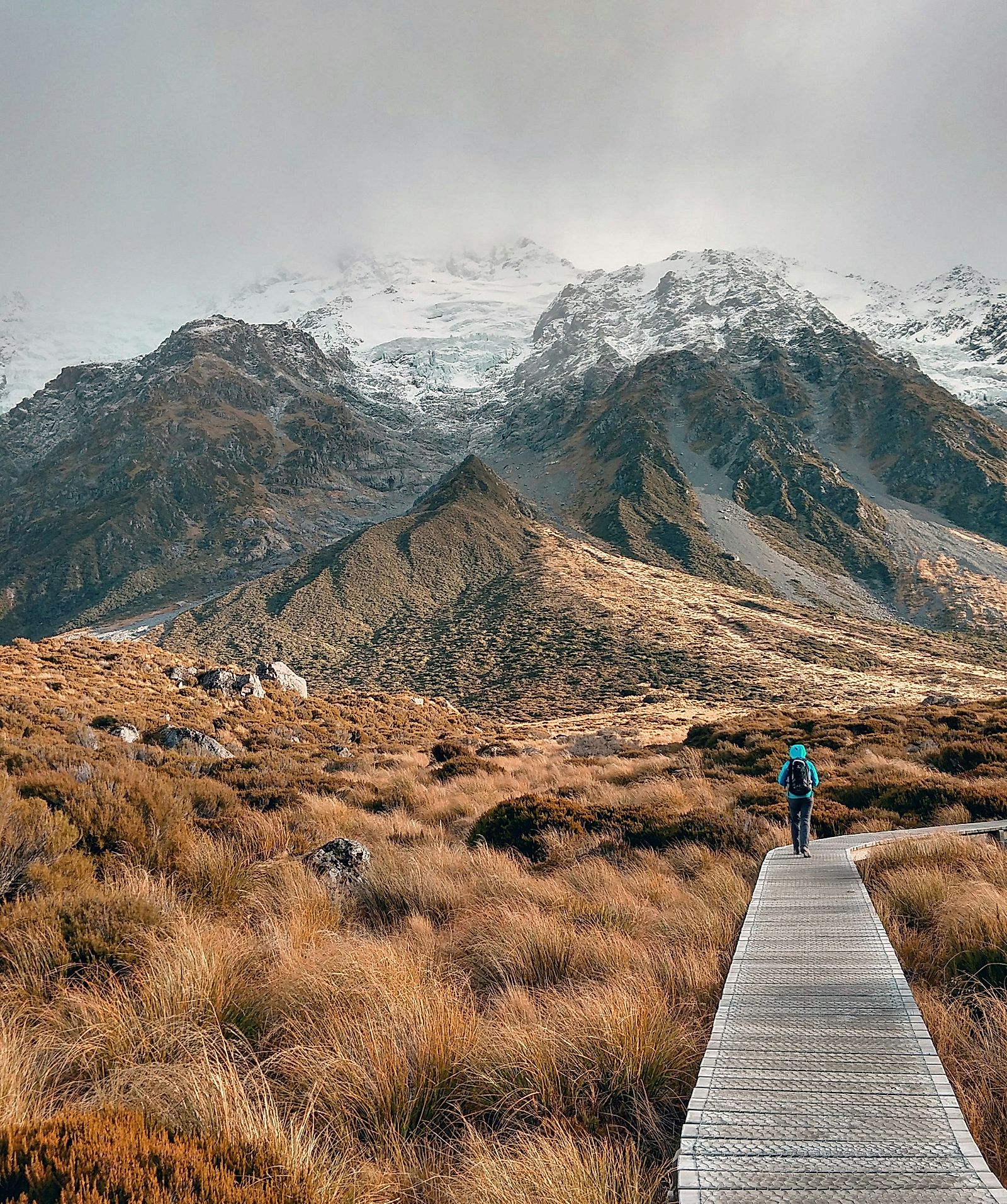 Person walking on wooden pathway near mountain.